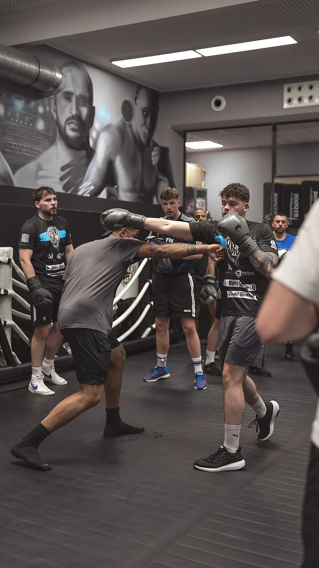 Trainer Philipp zeigt eine Boxkombination am Partner, die Gruppe schaut zu