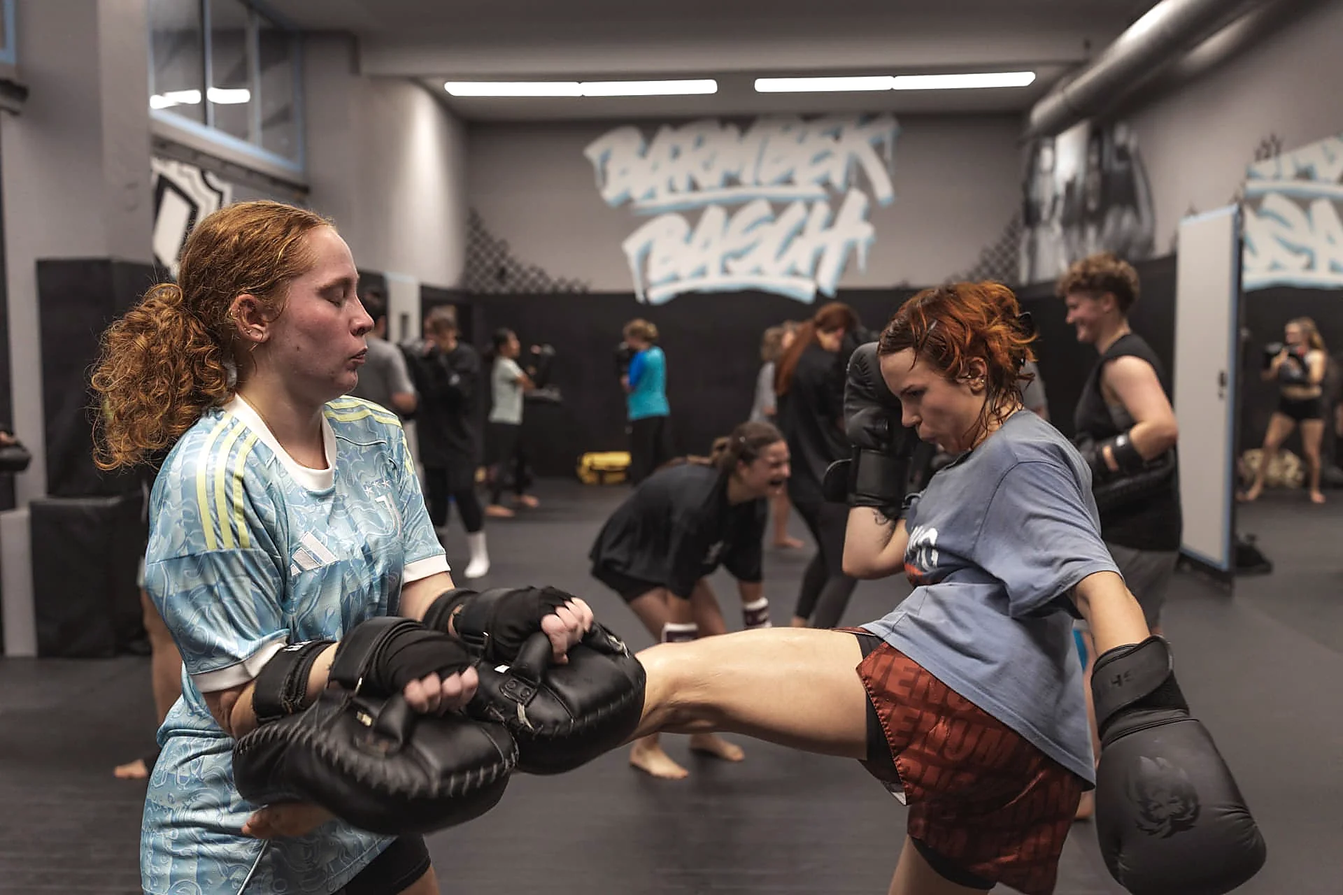 Kickboxerin tritt im Ladies-Kurs auf die Pratzen, im Hintergrund die Gruppe