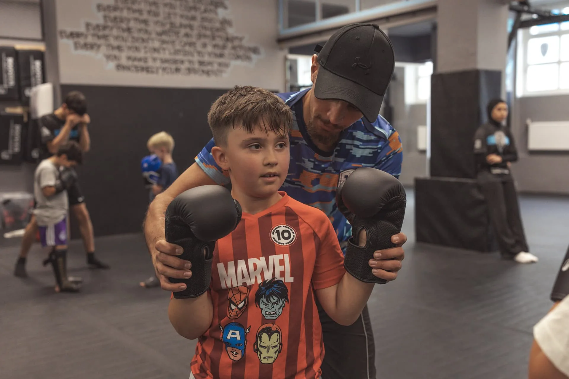 Trainer korrigiert einem Jungen von hinten die Deckung im Kindertraining