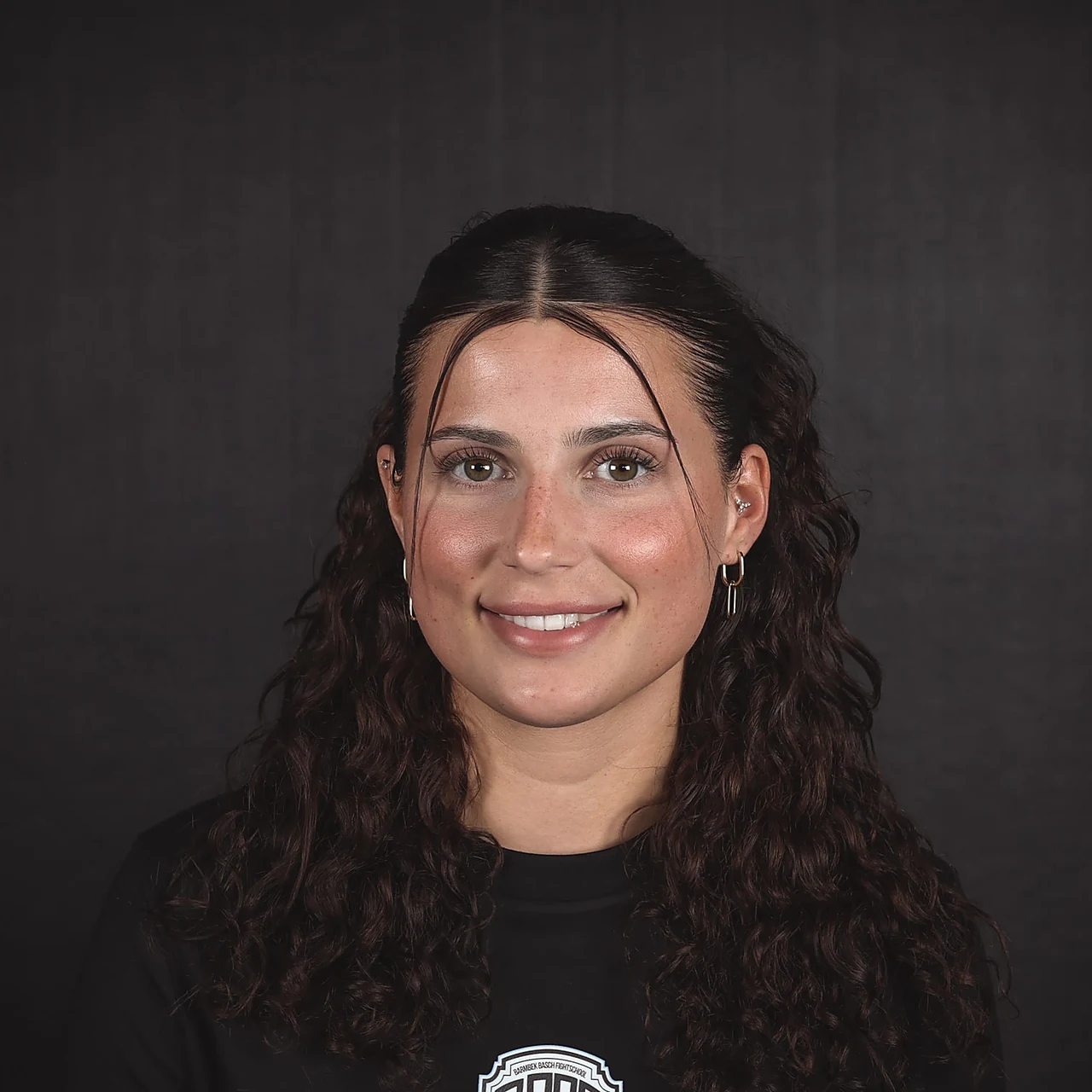 Annie, Deutsche Meisterin 2024 der WAKO im K1 bis 65 kg, lächelnd im Porträt mit Vereins-Shirt der Barmbek Basch Fightschool