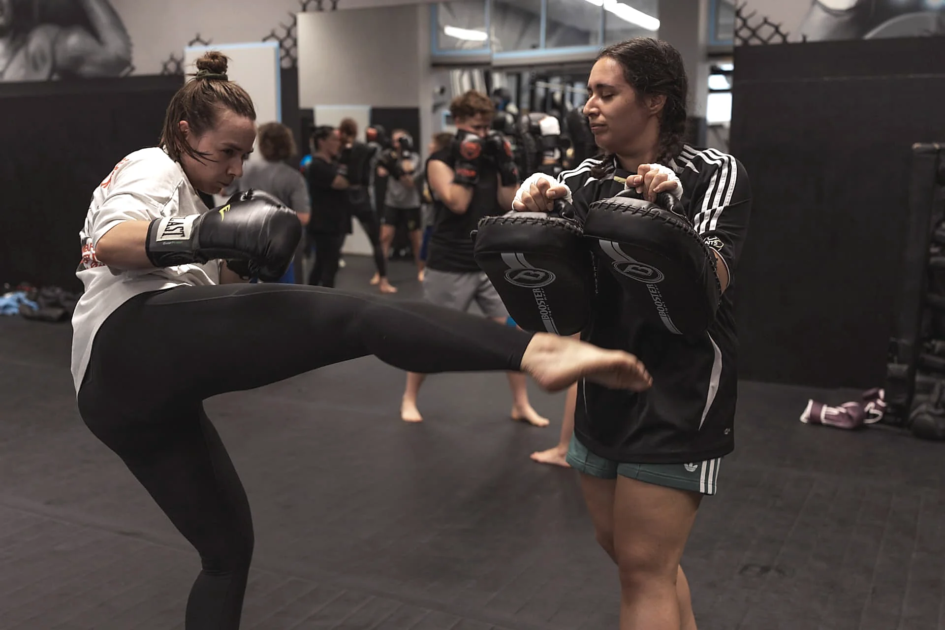 Frau tritt einen Frontkick auf die Pratzen ihrer Trainingspartnerin