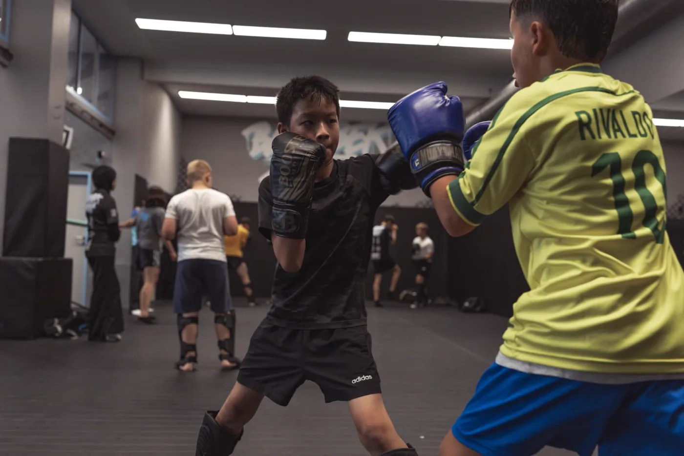Zwei Kinder üben im leichten Sparring mit Handschuhen und Schienbeinschonern