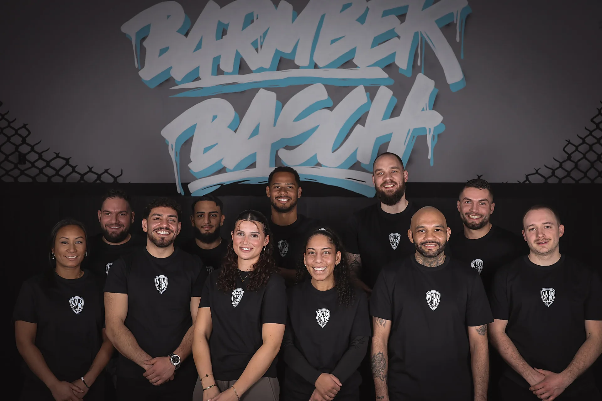 Das Team der Barmbek Basch Fightschool lächelt vor dem BARMBEK-BASCH-Graffiti